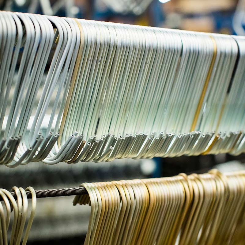 Close-up view of silver-plated and gold-plated wire hooks hanging in organized rows along industrial rack plating fixtures at Plateco.